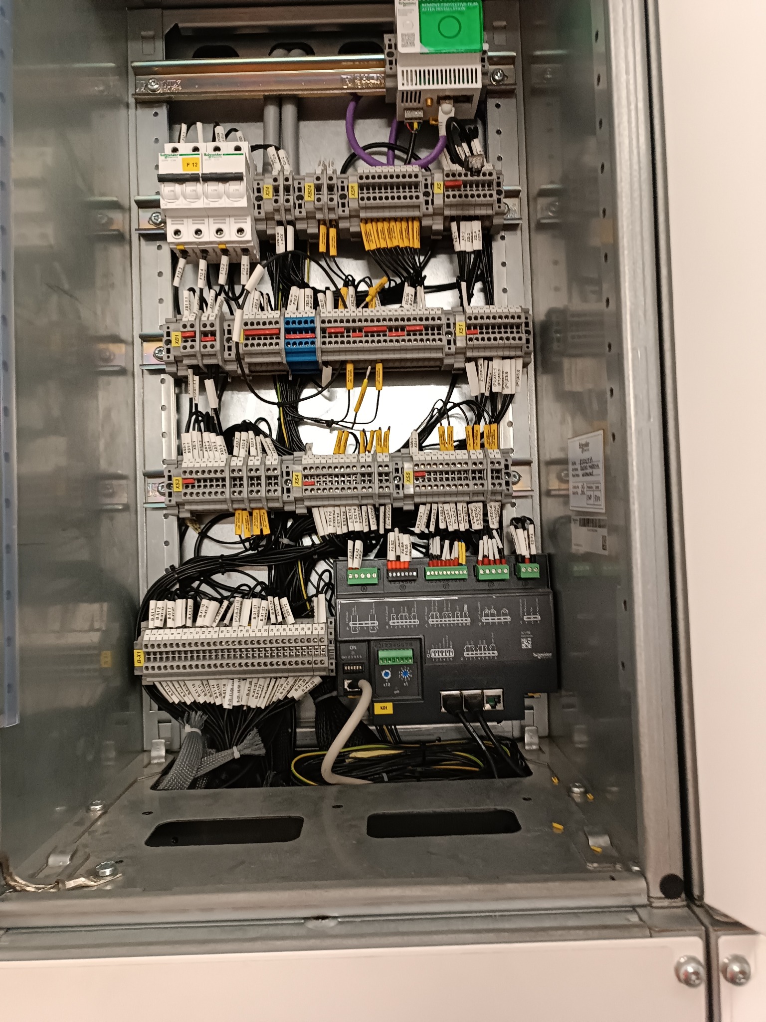 Wewnętrzny widok szafy sterowniczej z licznymi przewodami, złączkami i modułami elektronicznymi. Widoczne oznaczenia na przewodach i elementach, charakterystyczne dla instalacji elektrycznych.