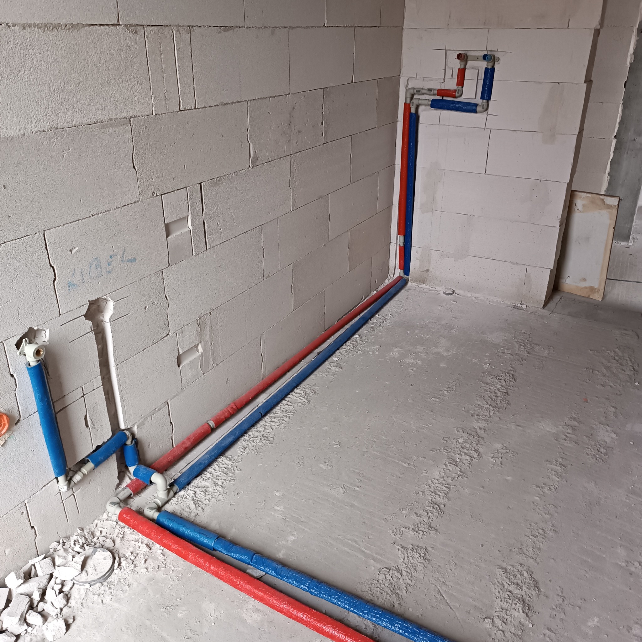 Instalacja wodna z rur PEX w kolorach czerwonym i niebieskim, zamontowana na surowych ścianach z betonu komórkowego w trakcie remontu łazienki.