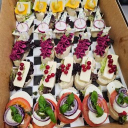 Pracownia Smaku - Różnorodne kanapeczki na pieczywie w kartonowym pudełku: ser żółty, pleśniowy, mozzarella z pomidorem i bazylią, dekorowane rzodkiewką, kwiatami i czerwoną porzeczką.