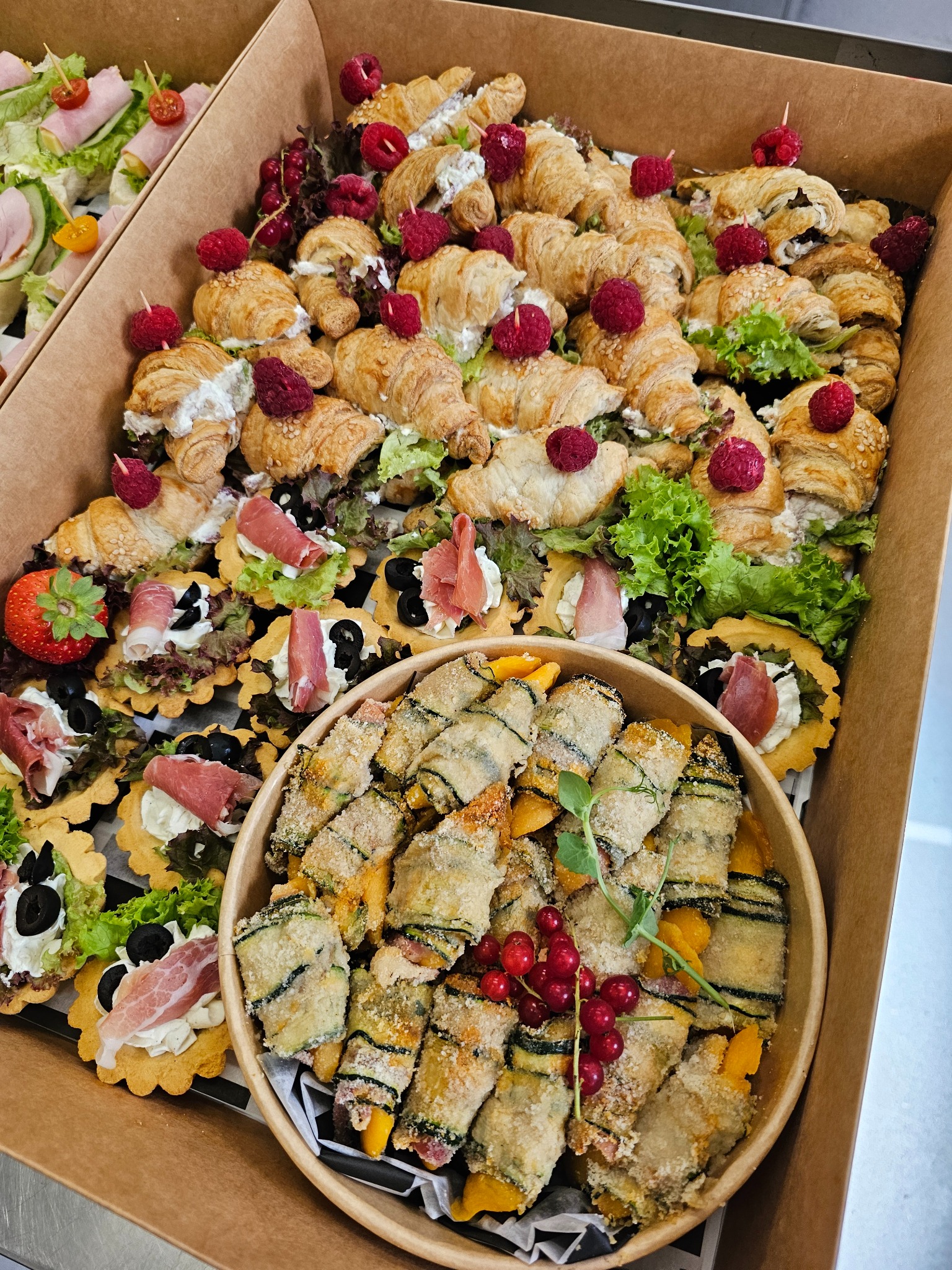 Elegancki catering: tarta z szynką, roladki z cukinii i croissanty z malinami w kartonowym pudełku. Różnorodność przekąsek na przyjęcie, widok z góry.