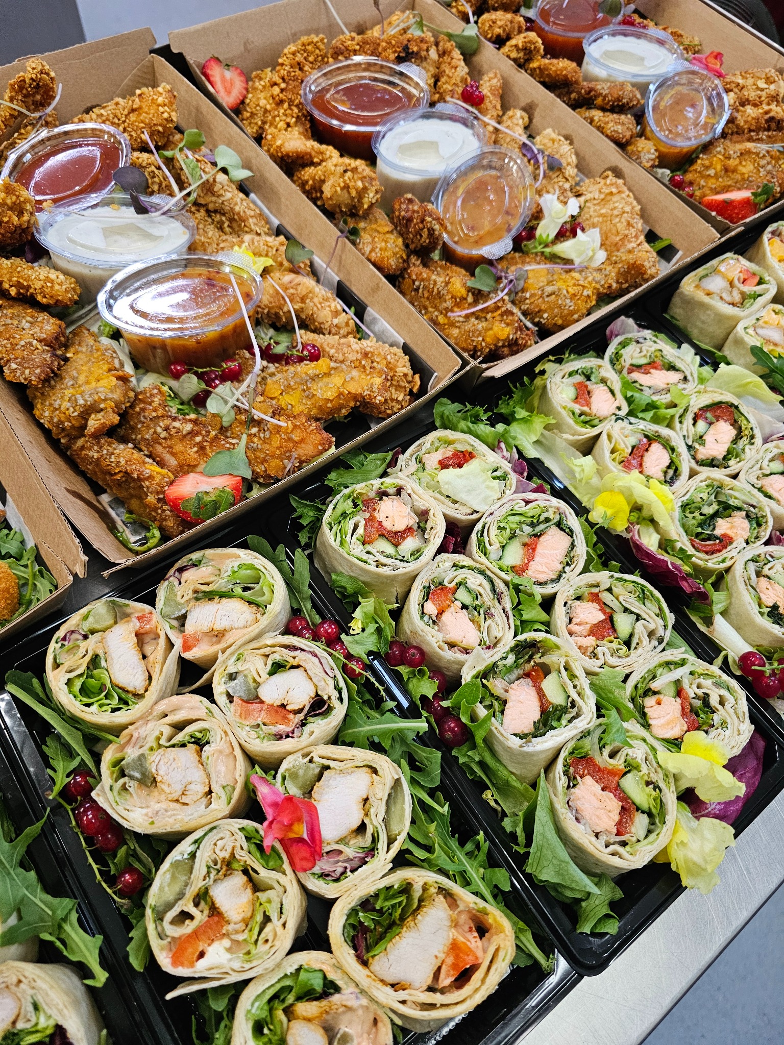 Zestaw cateringowy: roladki z kurczakiem i łososiem, nuggetsy w panierce z sosami, dekorowane zieleniną i owocami. Eleganckie pudełka i tace.