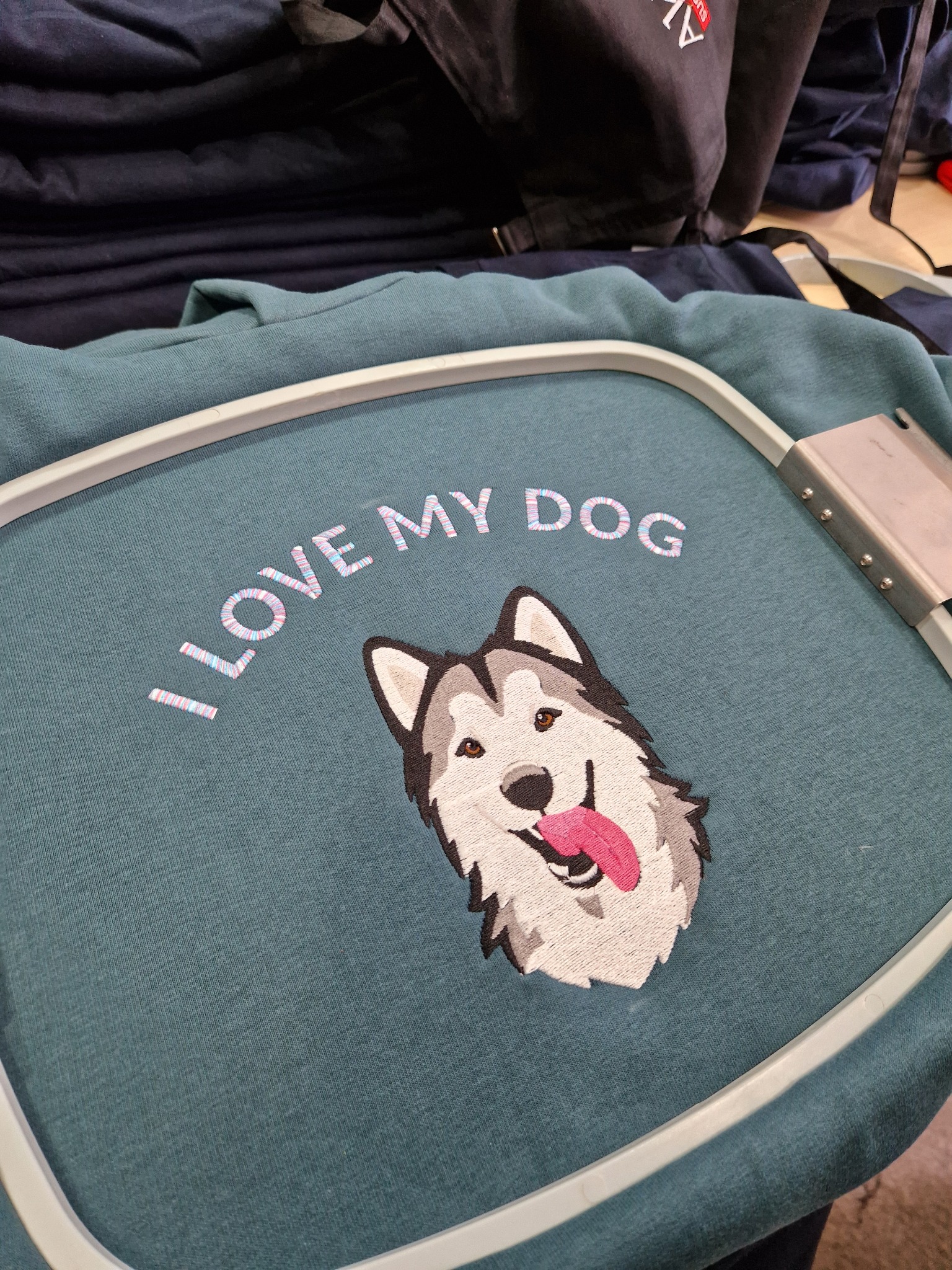 Bluza w tamborku z haftem przedstawiającym głowę psa rasy husky i napisem 'I LOVE MY DOG'. Widoczny fragment maszyny do haftowania.