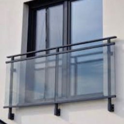 Mono-Steel - Nowoczesna balustrada szklana balkonu z czarnymi, metalowymi elementami mocującymi, widoczna na tle jasnej elewacji budynku i okna balkonowego.