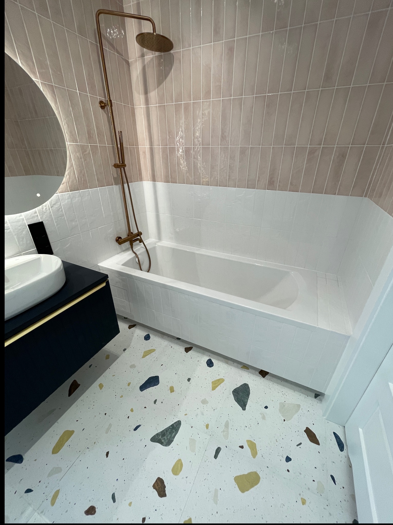 Nowoczesna łazienka po remoncie: beżowe płytki ścienne, biała wanna obudowana płytkami, umywalka na szafce i podłoga w stylu lastryko.