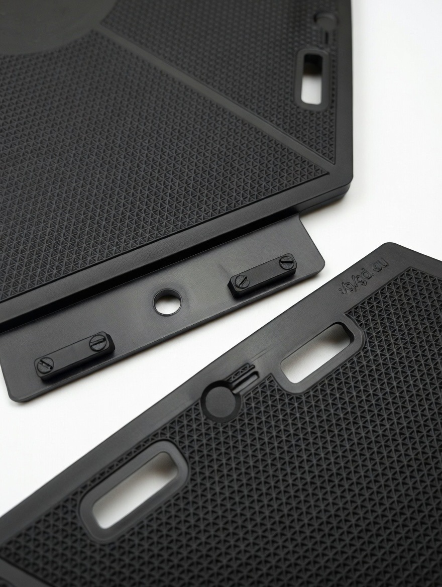 Czarne, teksturowane panele podłogowe z widocznymi mocowaniami i otworami, ułożone na białym tle. Detal montażowy paneli podłogowych.