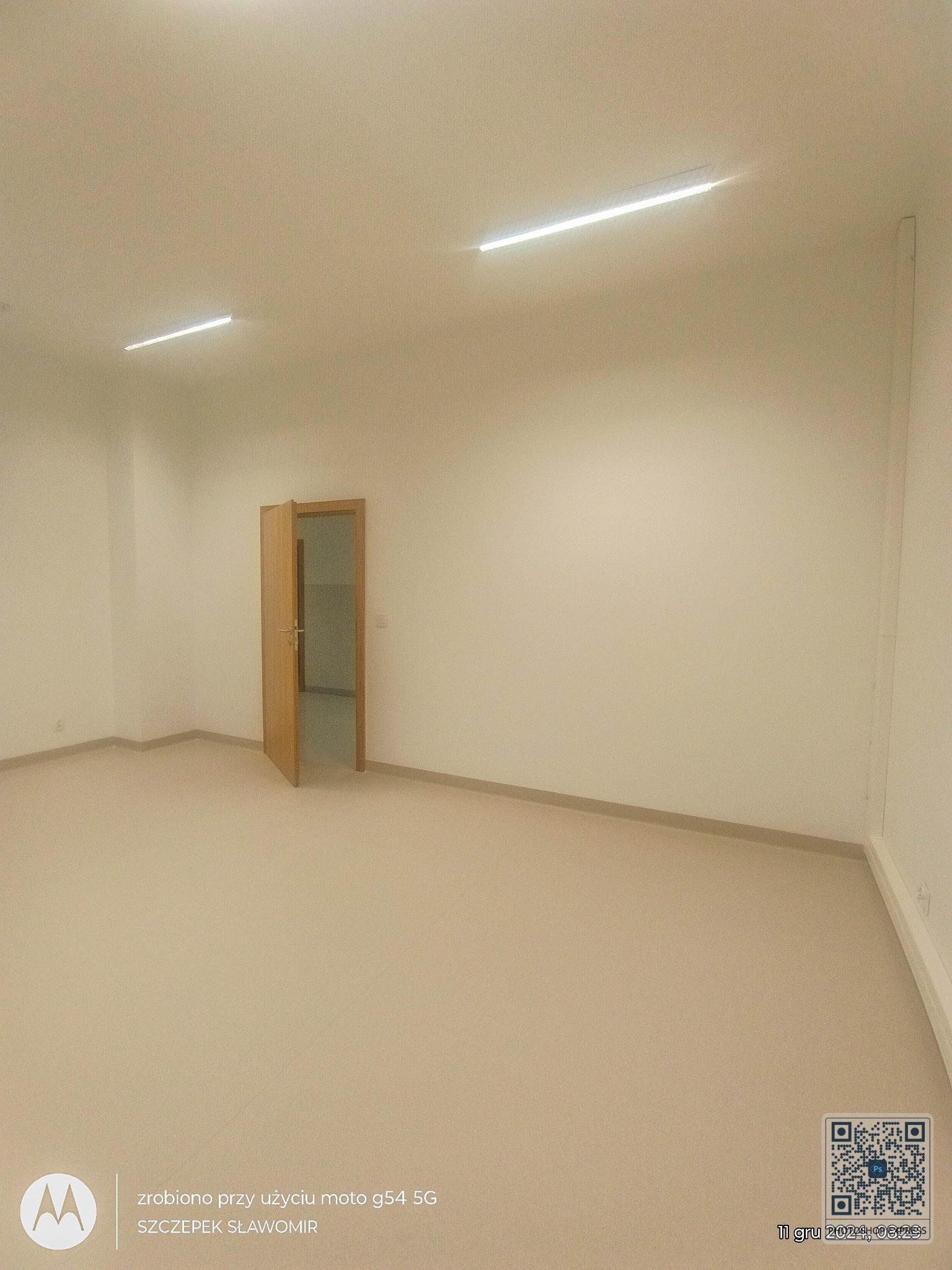 Puste, jasne wnętrze po remoncie z otwartymi drewnianymi drzwiami. Widoczne proste oświetlenie sufitowe i kremowe ściany. Minimalistyczny styl wykończenia.