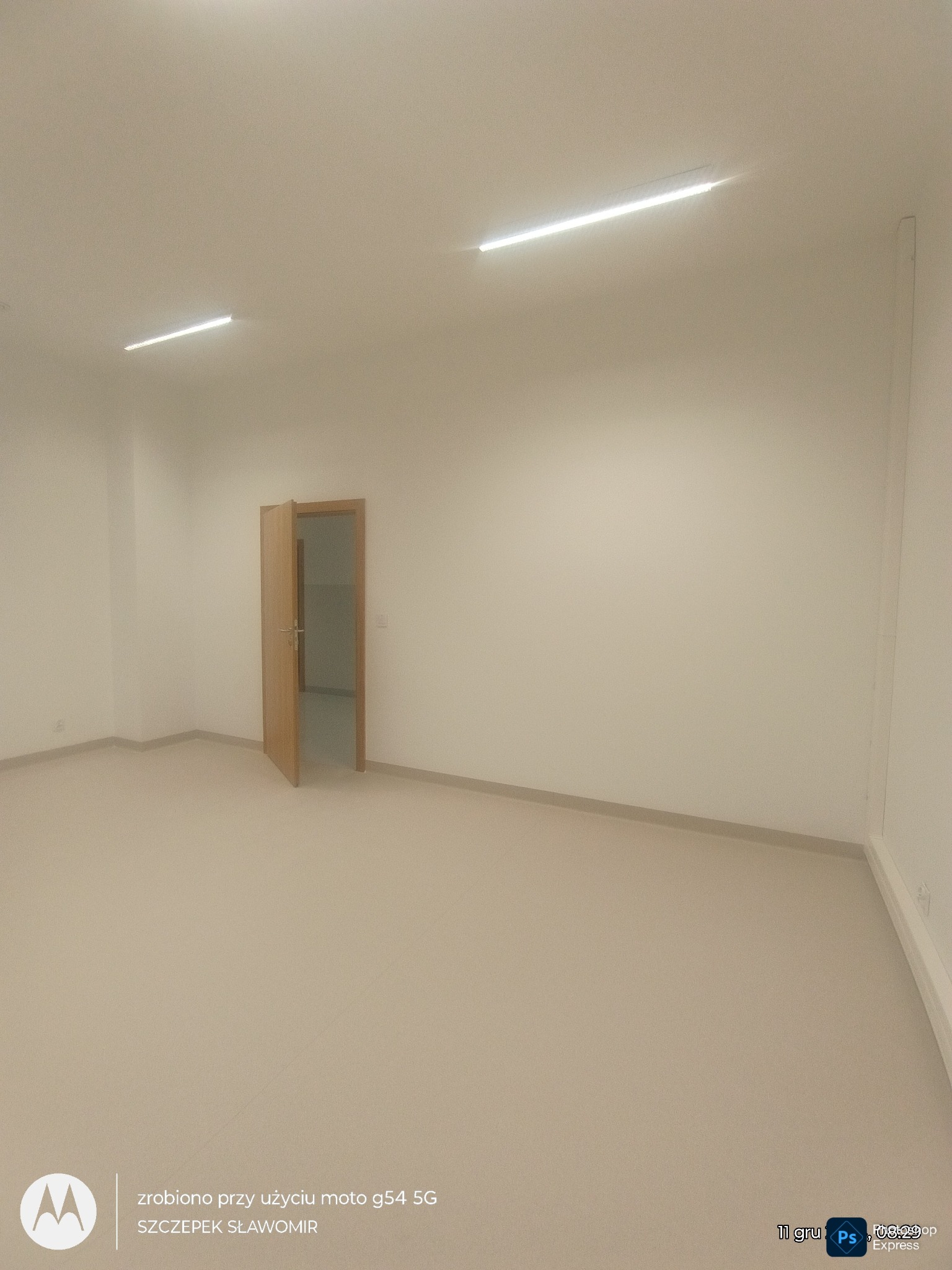 Jasne, odnowione wnętrze z otwartymi drzwiami, widoczne oświetlenie sufitowe. Ściany w neutralnym odcieniu, podłoga wykończona w beżowym kolorze. Minimalistyczny design.