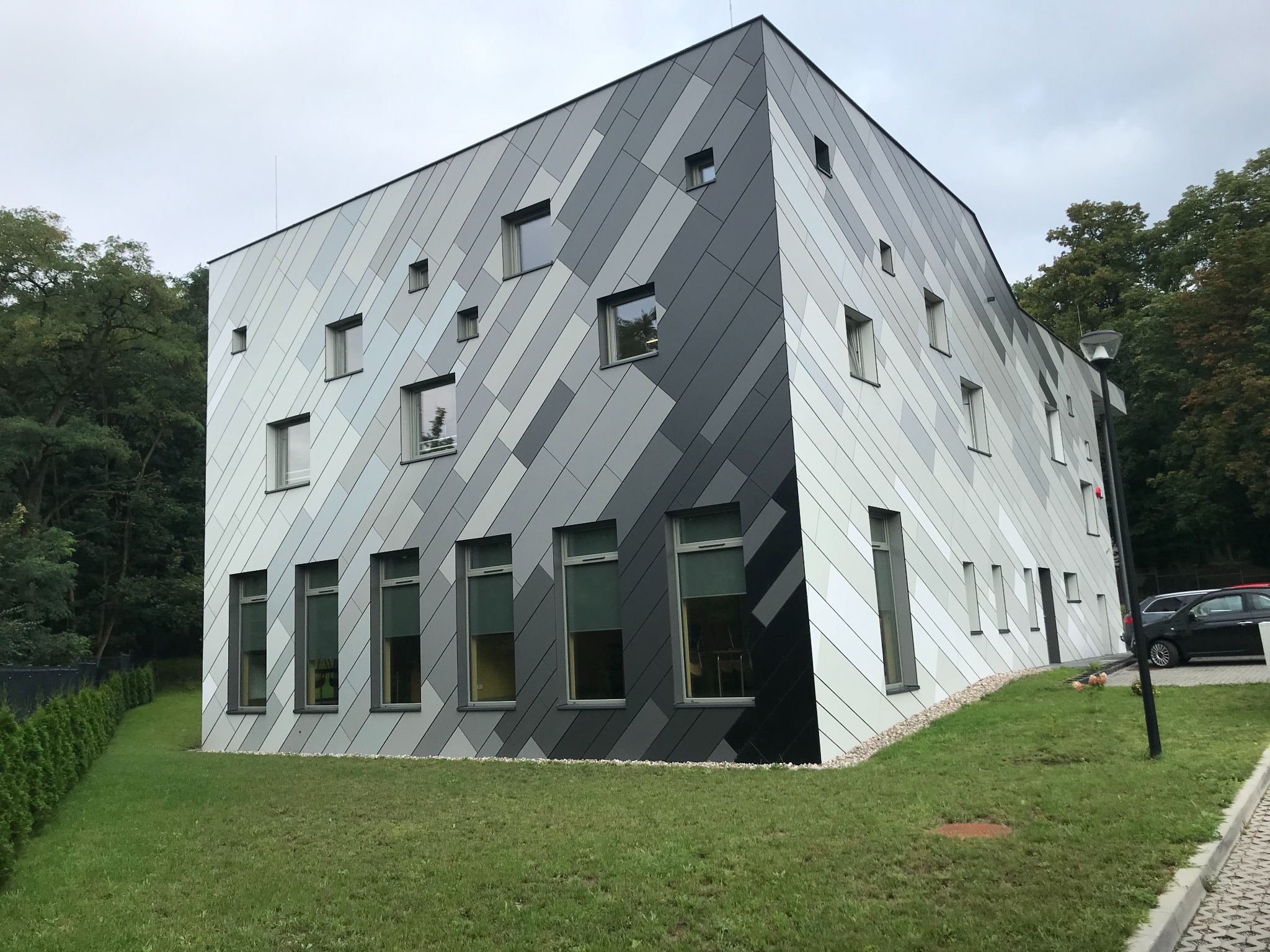 Nowoczesny budynek Szkoły Specjalnej w Lipnie z elewacją w odcieniach szarości, z licznymi oknami o różnych rozmiarach, otoczony zielenią i drzewami.