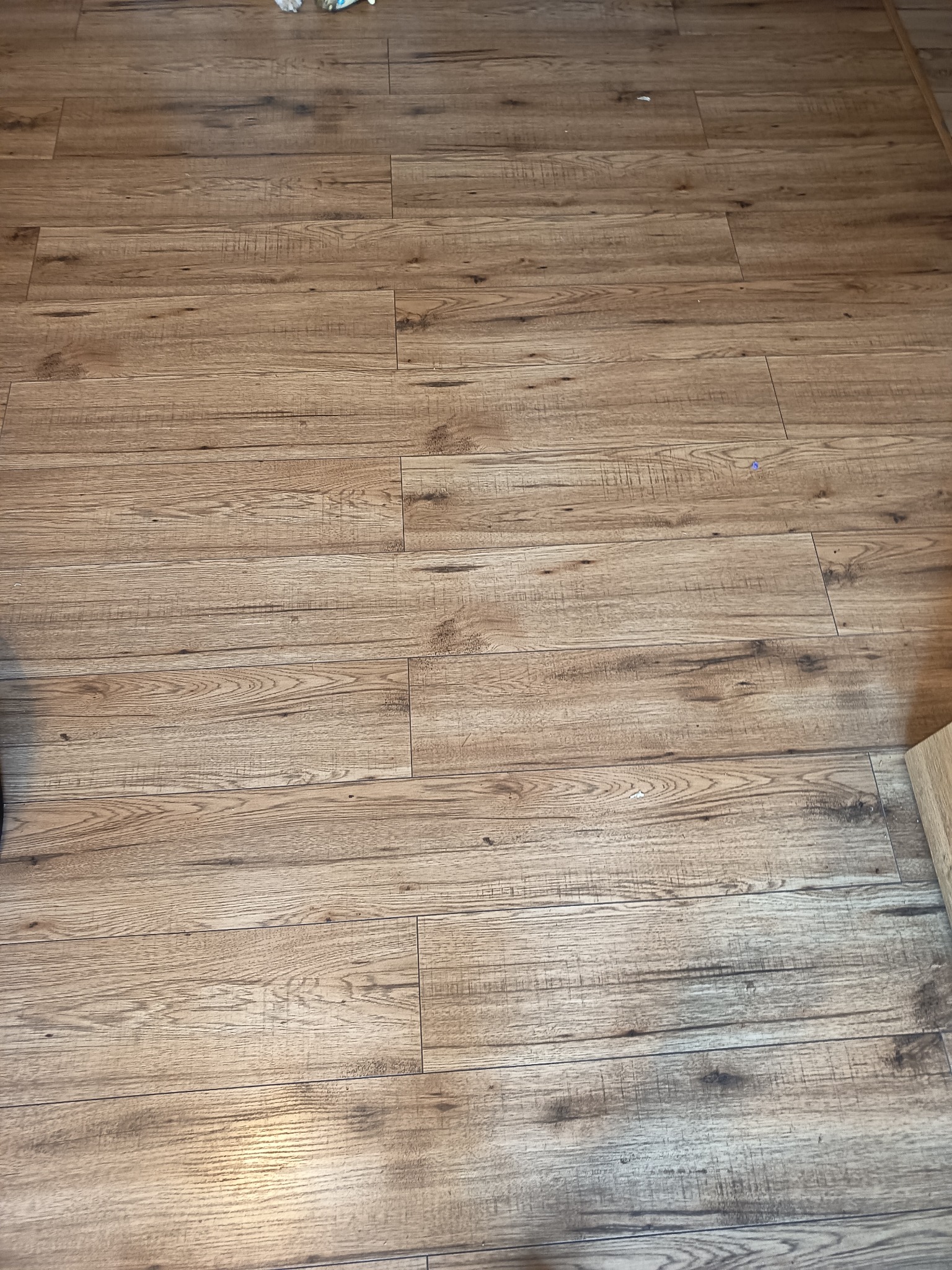 Jasne, drewnopodobne panele podłogowe ułożone w regularny wzór, z widoczną fakturą drewna i delikatnymi przebarwieniami. Ujęcie z góry, fragment podłogi.