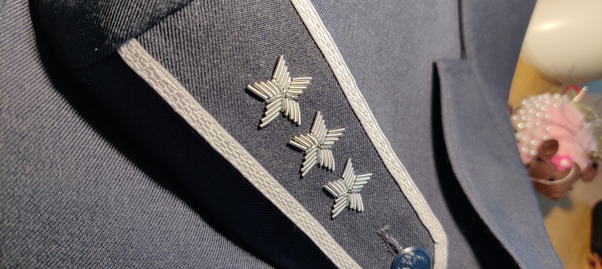 Granatowa marynarka z naszytymi trzema srebrnymi gwiazdami i ozdobnym obszyciem, widoczny guzik. Detal odzieży męskiej.