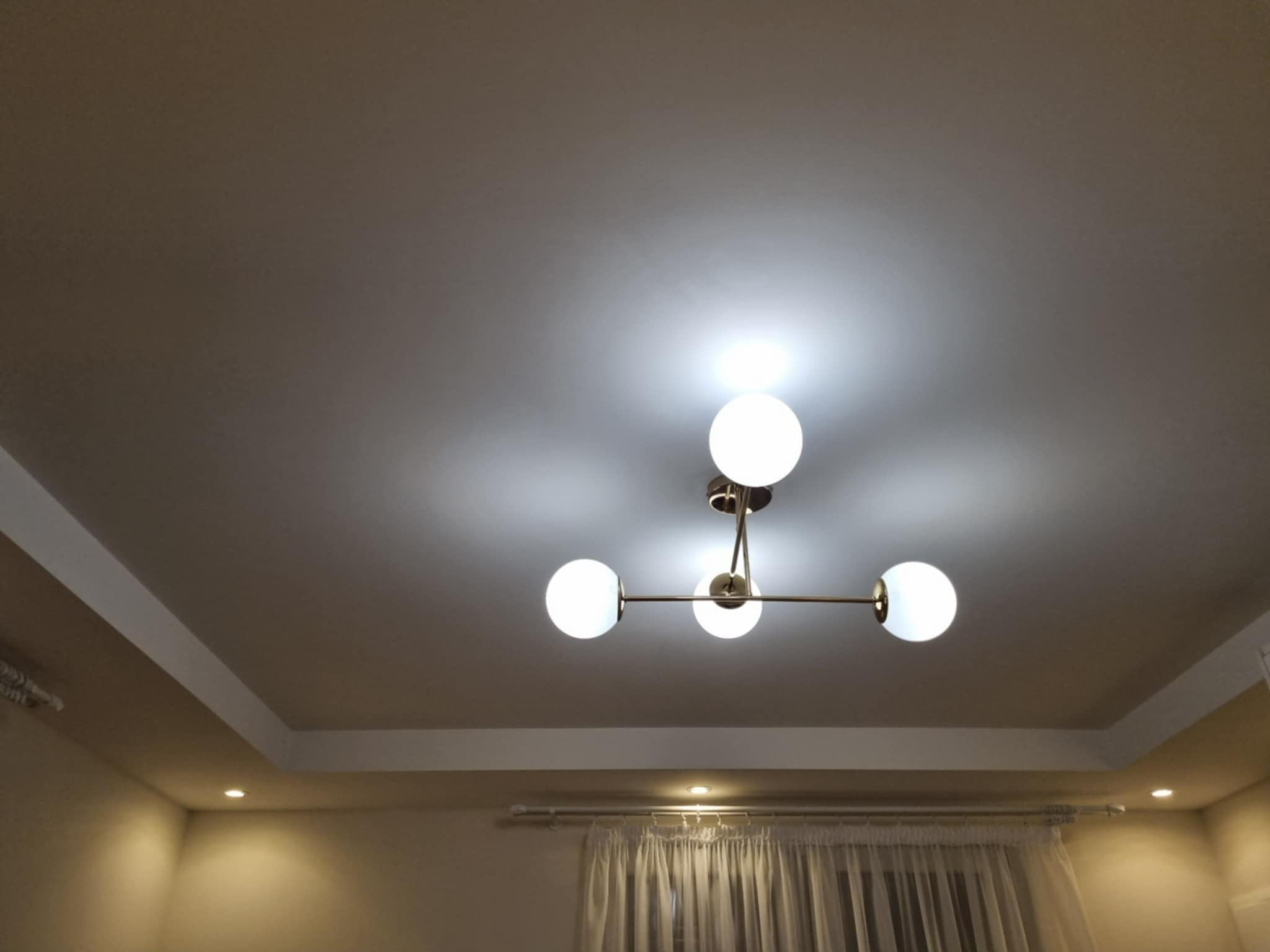 Nowoczesny sufit podwieszany z oświetleniem punktowym i designerską lampą wiszącą z kulistymi kloszami. Jasne wnętrze.