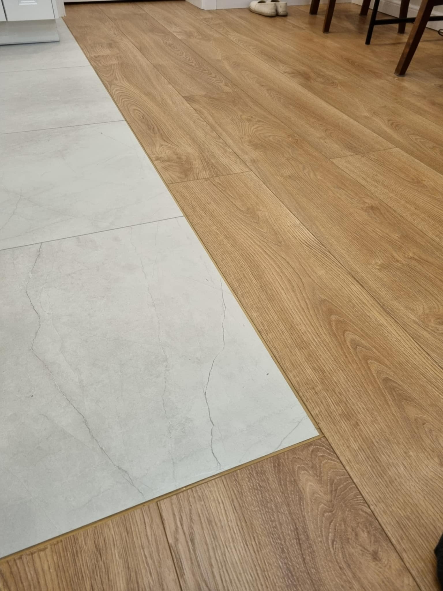 Połączenie podłogi z paneli drewnopodobnych i płytek ceramicznych imitujących marmur. Widoczna listwa progowa i fragment mebli.