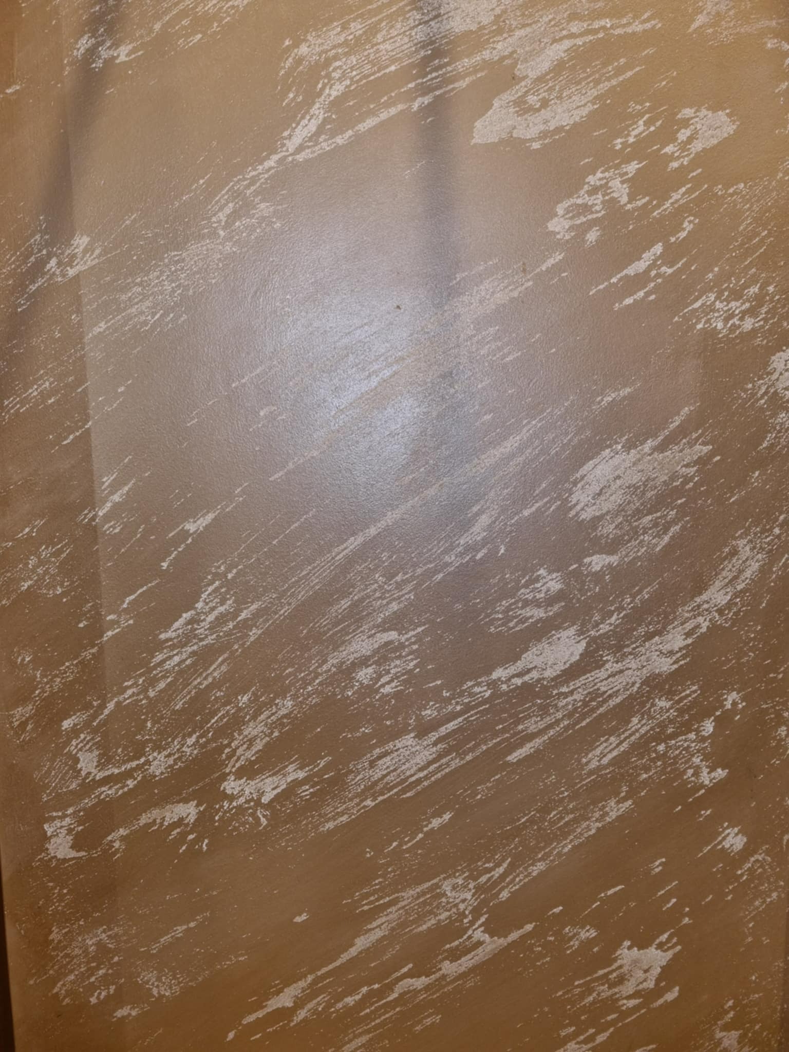 Dekoracyjna ściana w odcieniach brązu z nieregularnymi, jasnymi smugami, imitującymi efekt przetarcia. Widoczne delikatne refleksy świetlne na powierzchni.