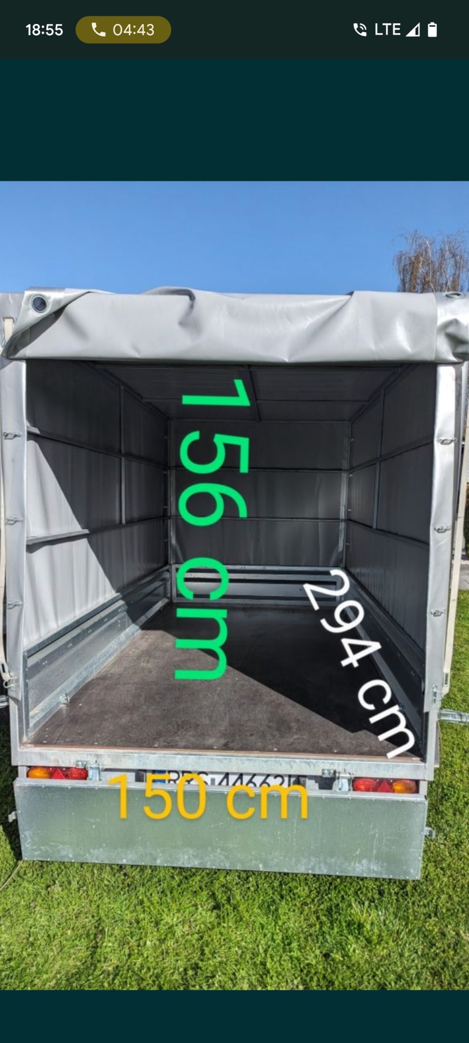Wnętrze przyczepy transportowej z plandeką, wymiary: 156 cm (wysokość), 294 cm (długość), 150 cm (szerokość). Widok z tyłu, na zielonym tle trawy.
