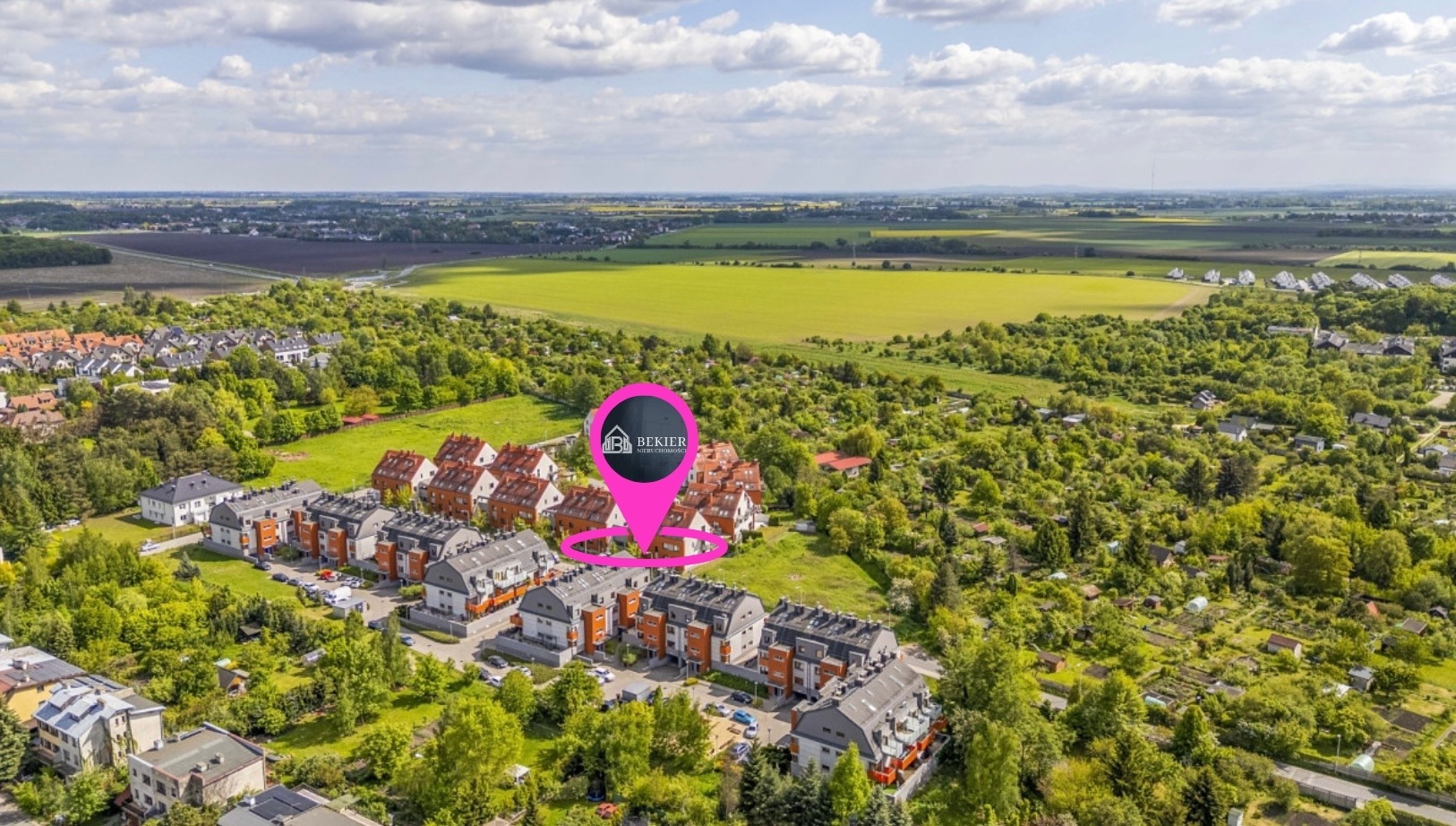 Panoramiczny widok osiedla domów z lotu ptaka, z zielonymi terenami i oznaczeniem lokalizacji firmy Bekier Nieruchomości.