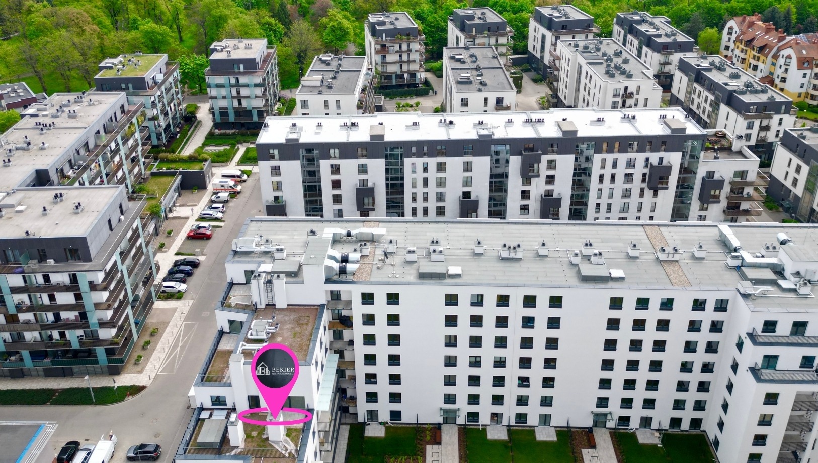 Kompleks nowoczesnych apartamentowców z zielonymi dachami, widok z lotu ptaka, oznaczony lokalizator z logo agencji nieruchomości.