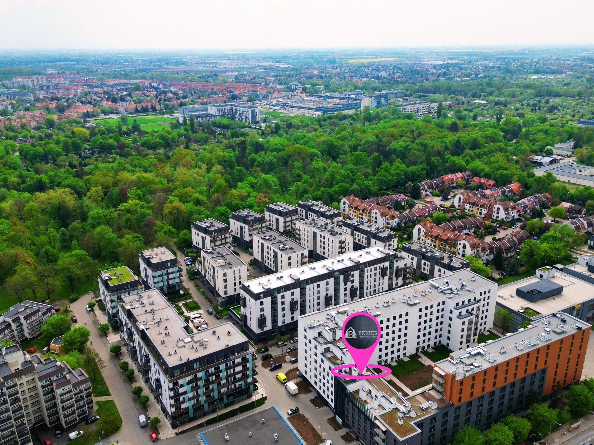 Aerial view of modern apartment buildings with green roofs and a pink location pin indicating a real estate agency in a residential area.
