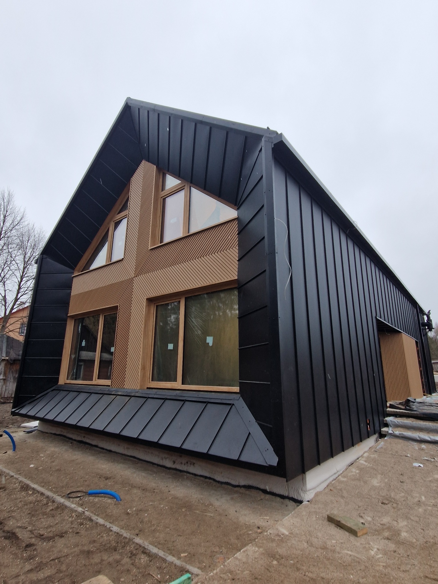 Nowoczesny dom z czarnym metalowym dachem i drewnianą elewacją, widok z dołu, podkreślający unikalną architekturę i wykończenie.