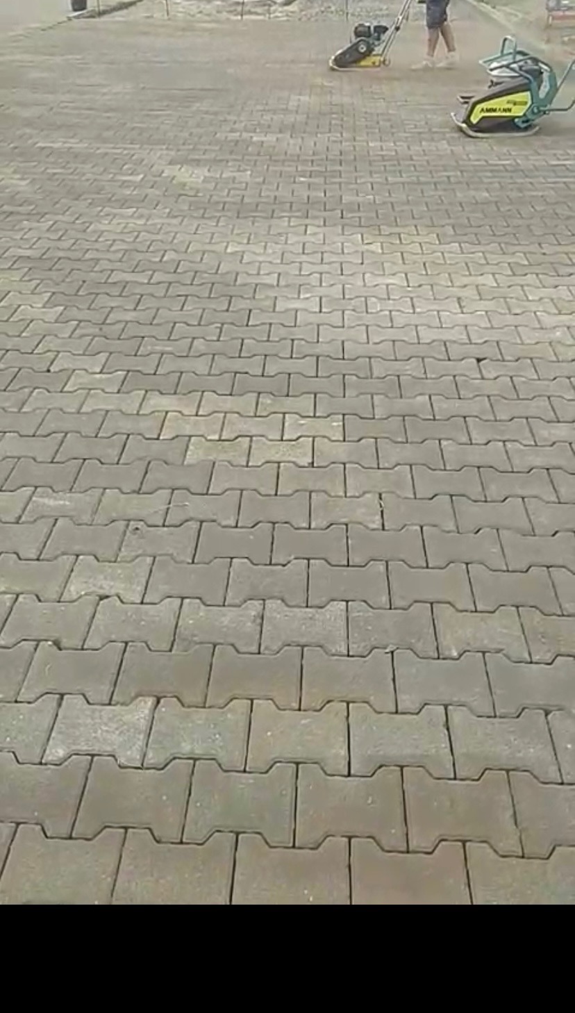 Układanie szarej kostki brukowej typu I, zagęszczanej mechanicznie. W tle widoczne maszyny i pracownik.