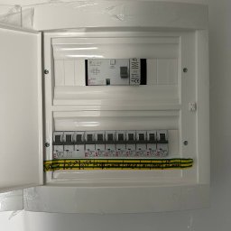 KR Instalbud - Otwarta, biała skrzynka bezpiecznikowa z zainstalowanymi bezpiecznikami ETI i przewodami z oznaczeniami, zamontowana na białej ścianie, widok z bliska.