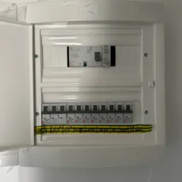 Otwarta, biała skrzynka bezpiecznikowa z zainstalowanymi bezpiecznikami ETI i przewodami z oznaczeniami, zamontowana na białej ścianie, widok z bliska.