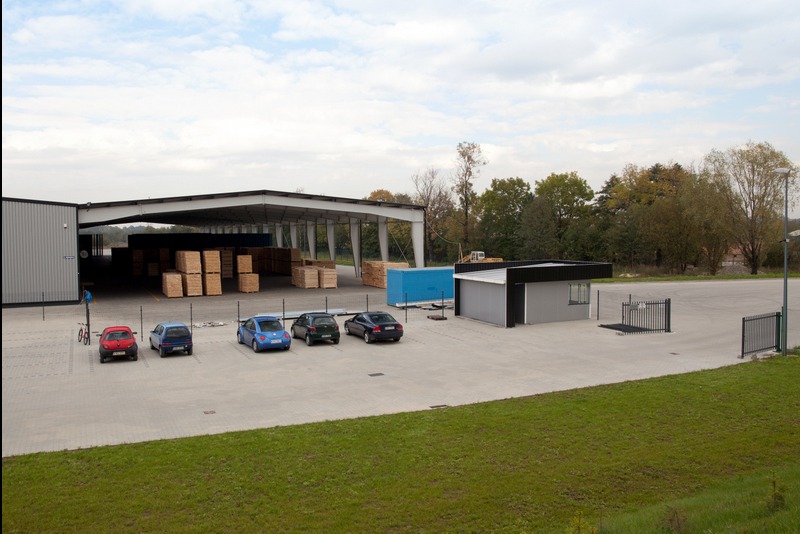 Hala magazynowa z konstrukcją stalową i zaparkowanymi autami. Widoczne drewniane palety składowane wewnątrz hali.