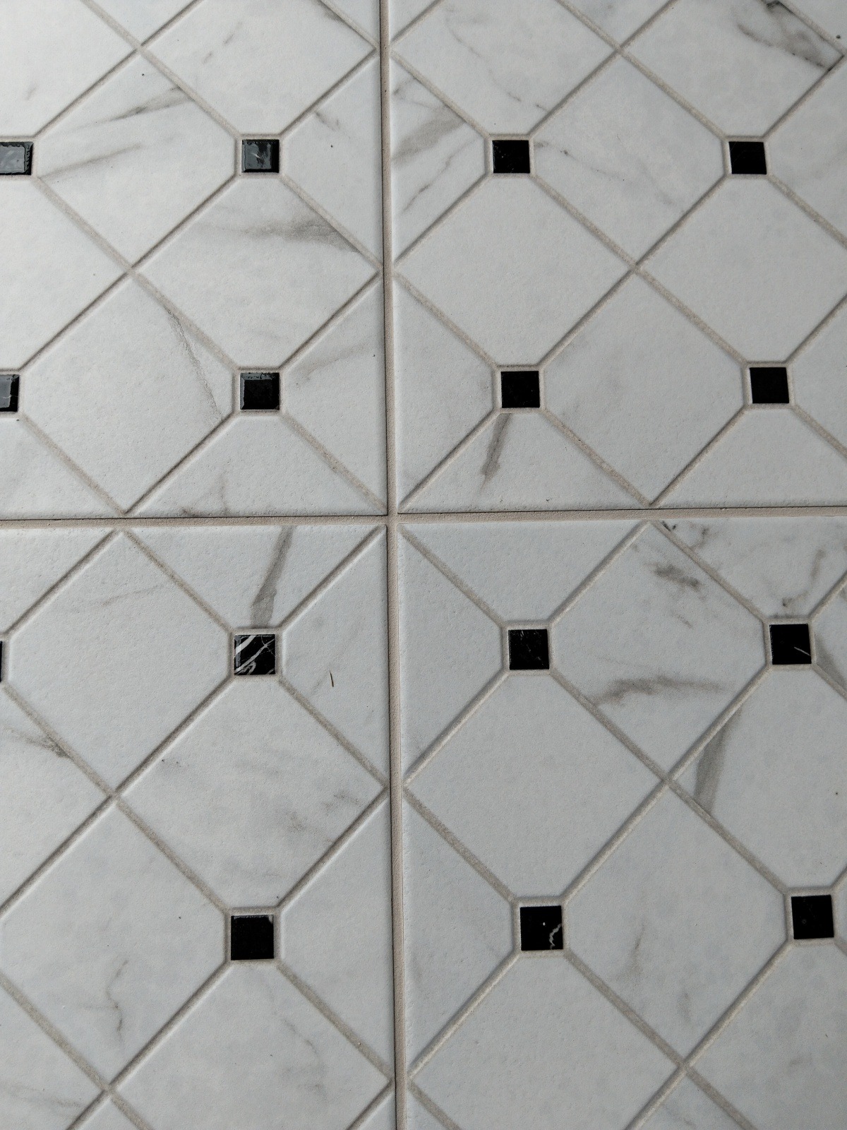 Ułożona podłoga z białych, marmurkowych płytek w romby z czarnymi kwadratami w środku. Widok z góry, fuga w odcieniu szarości, cztery płytki w kadrze.