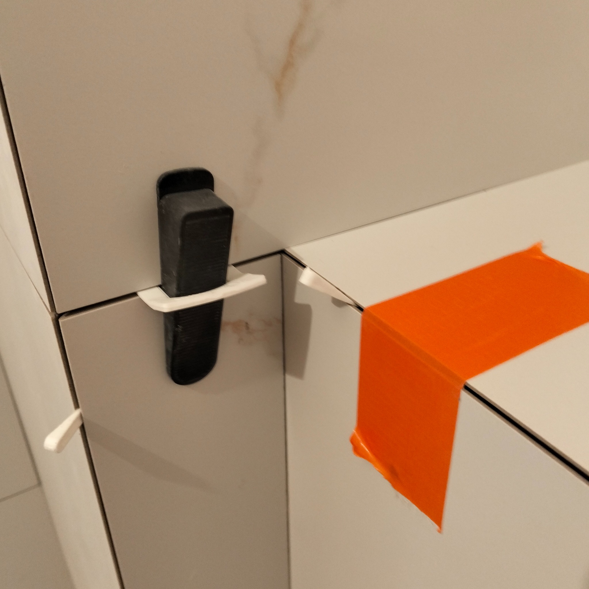 Precyzyjne układanie białych płytek z użyciem klipsów poziomujących i pomarańczowej taśmy maskującej, zapewniające równą powierzchnię. Detal wykończenia wnętrz.