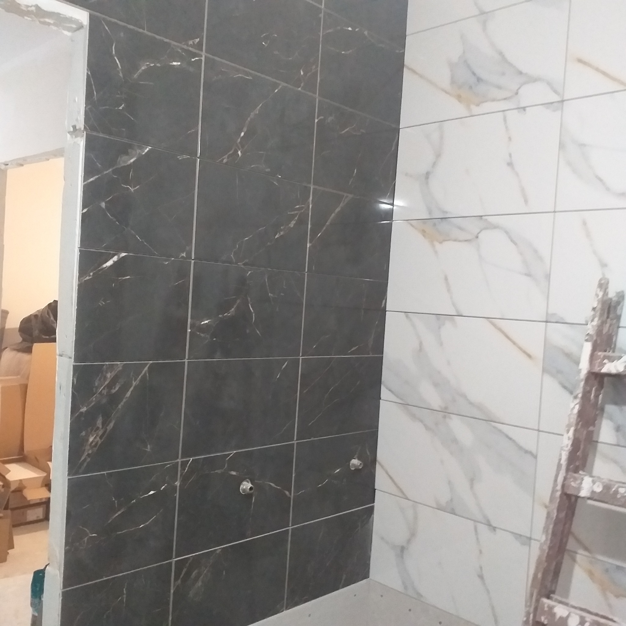 Ułożone, marmurowe płytki ścienne w łazience: czarne i białe. Widoczne rury instalacji wodnej i drabina malarska. Częściowo wykończone wnętrze.