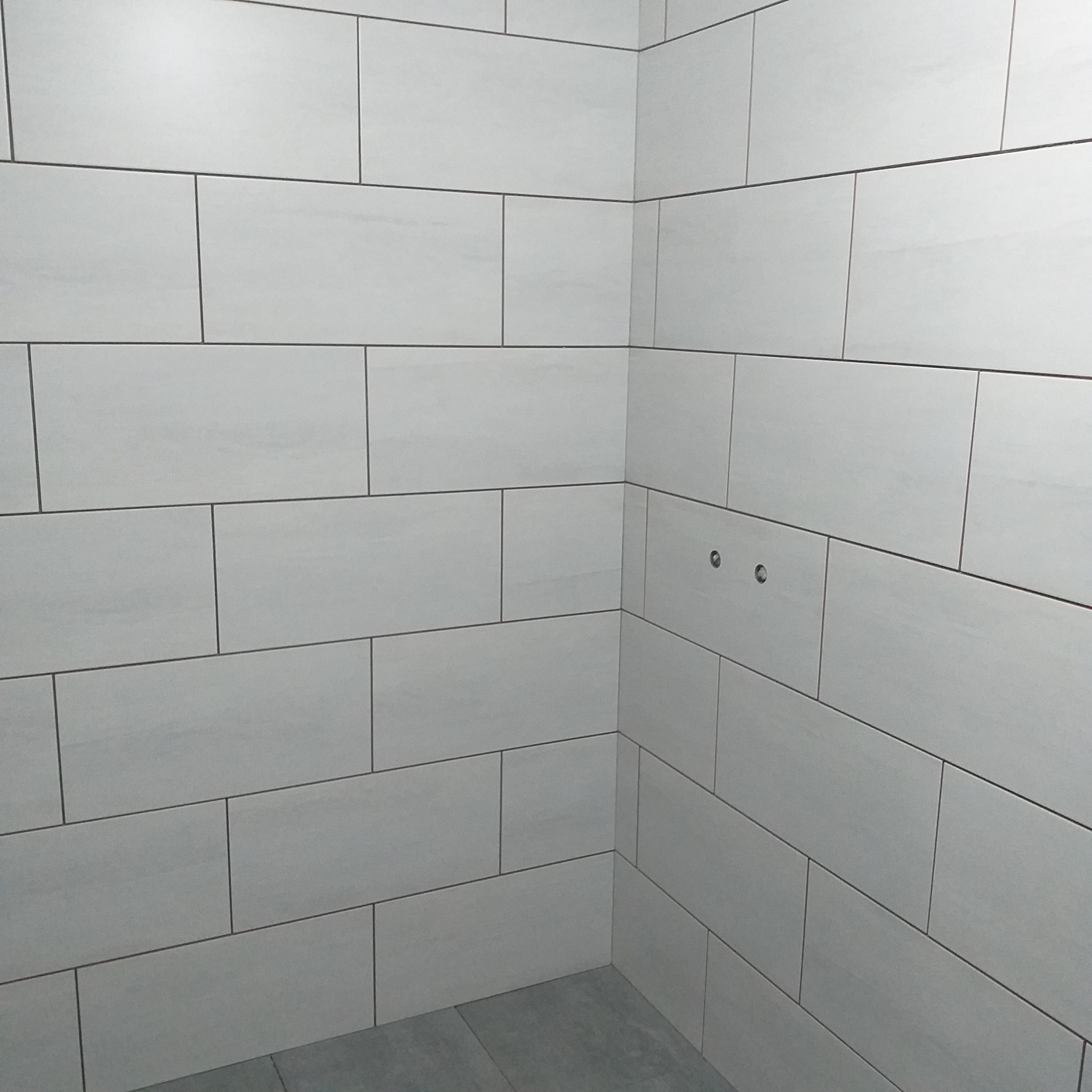 Wykończona ściana z białych, prostokątnych płytek w łazience w Zielonej Górze. Widoczne dwa otwory na baterię. Minimalistyczny styl i precyzyjne ułożenie glazury.