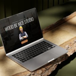 Ad Vision - Laptop prezentuje stronę 'Wood Be Nice Studio' na tle surowego drewna i zieleni. Ukazuje nowoczesny design i profesjonalizm stolarskiej pracowni.