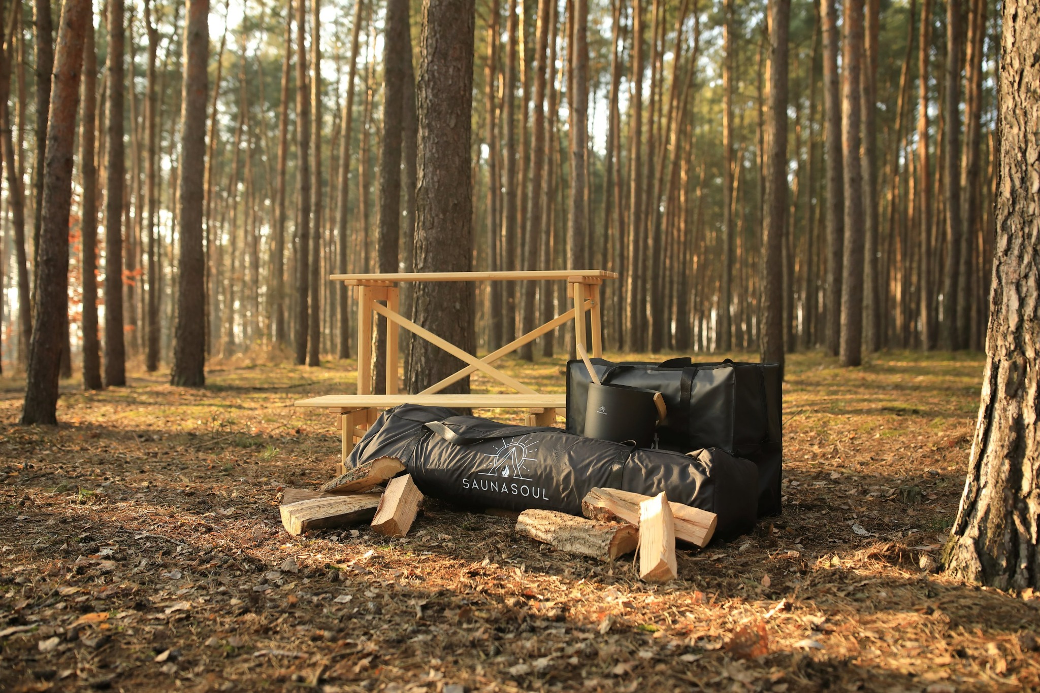 Przenośna sauna w lesie: rozłożone akcesoria, drewno, torby transportowe i ławka. Leśne otoczenie, ciepłe światło słoneczne, sprzęt do mobilnej sauny.