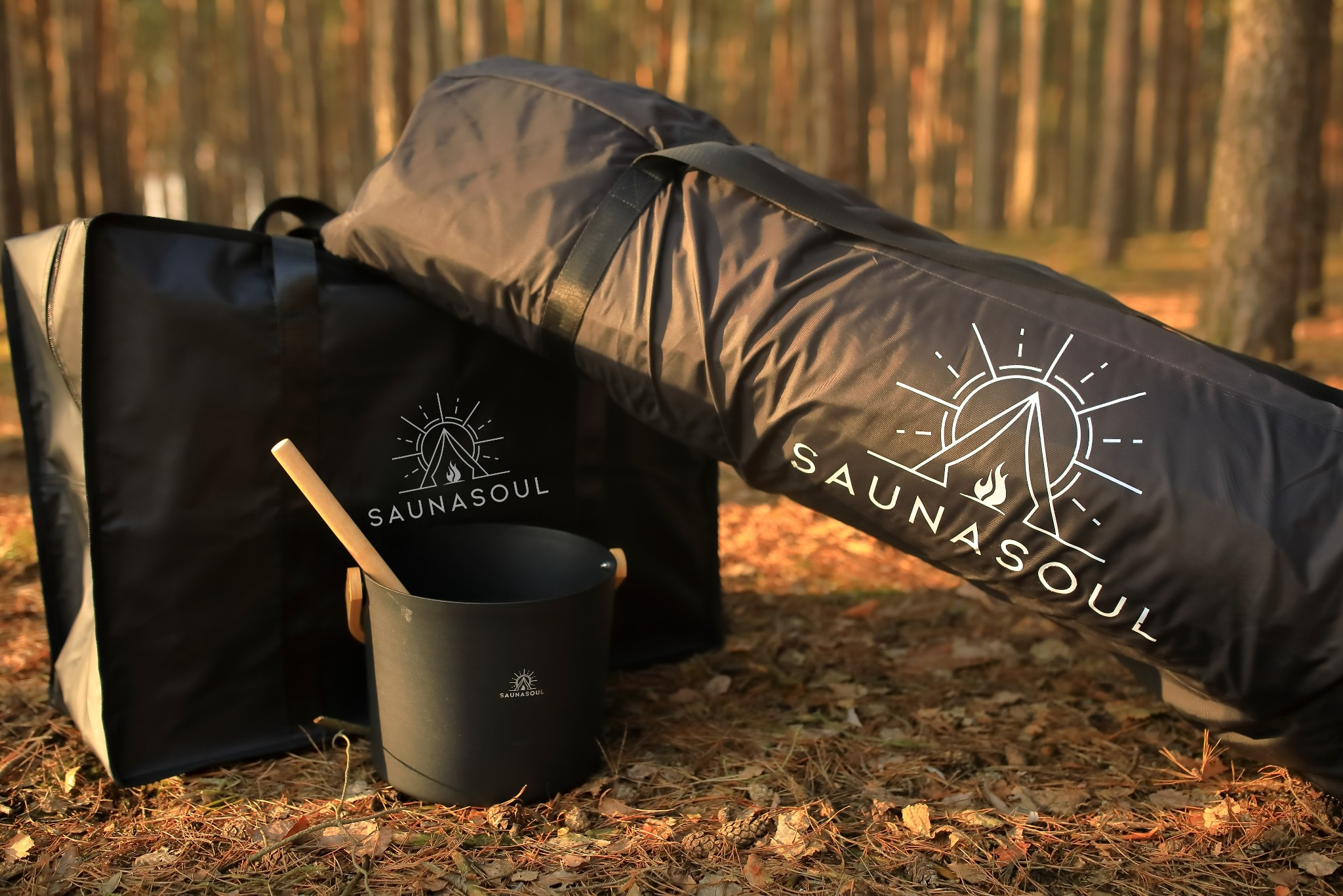 Zestaw akcesoriów do sauny mobilnej Saunasoul: torba, wiadro i chochla na tle leśnym. Minimalistyczny design z logo.