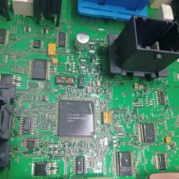 Zielona płytka drukowana z licznymi elementami elektronicznymi, w tym układami scalonymi, kondensatorami i złączami. Widoczne detale ścieżek i oznaczeń komponentów.