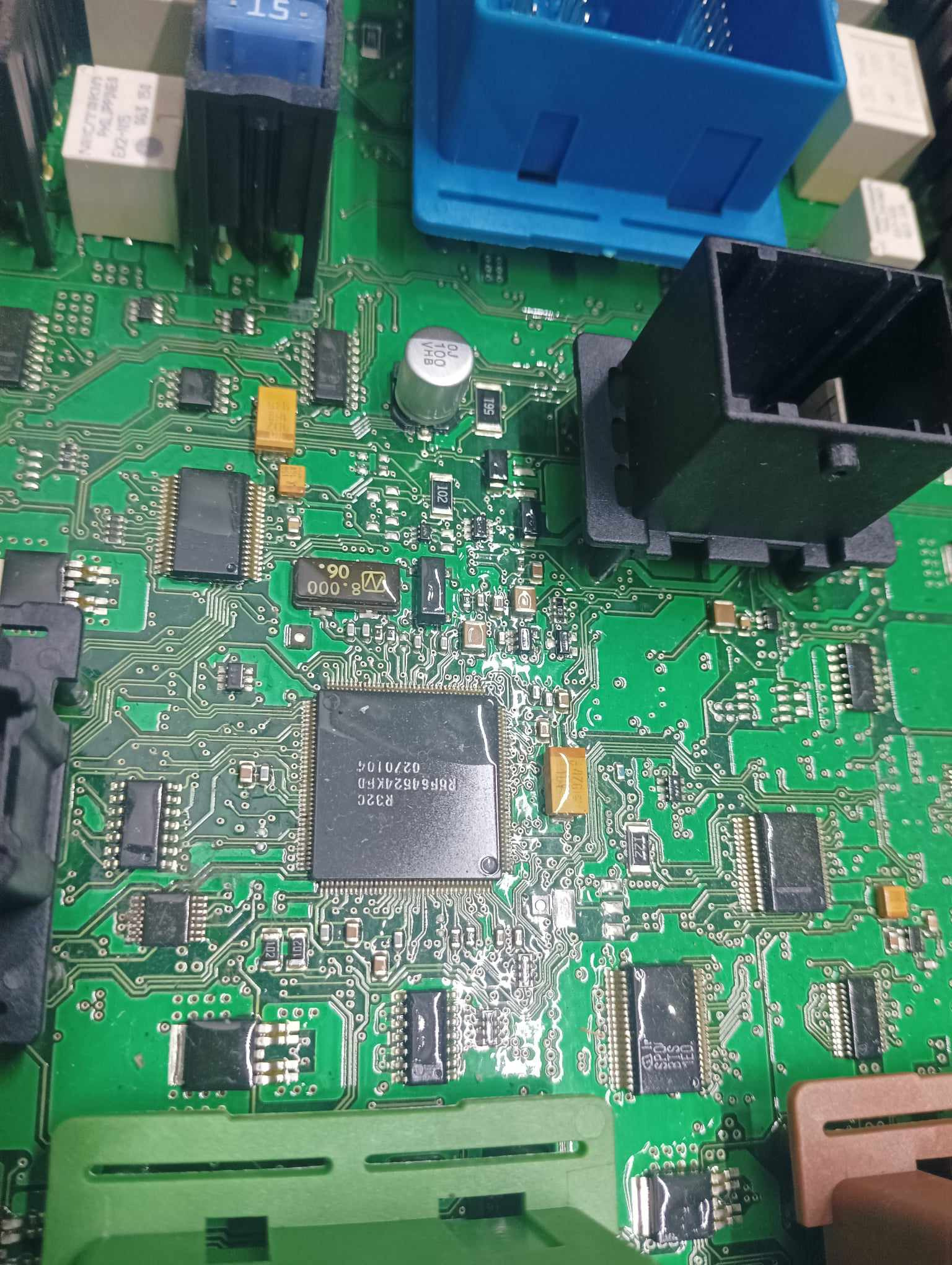 Zielona płytka drukowana z licznymi elementami elektronicznymi, w tym układami scalonymi, kondensatorami i złączami. Widoczne detale ścieżek i oznaczeń komponentów.