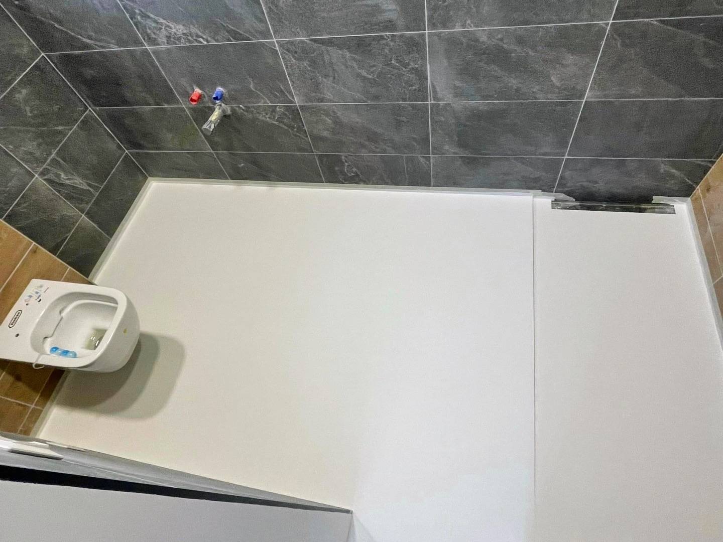 Biała posadzka żywiczna w łazience z szarymi płytkami i wiszącą toaletą. Widok z góry ukazuje gładką powierzchnię i minimalistyczny design.