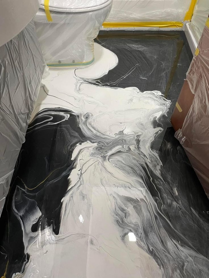 Czarno-biała posadzka z efektem marmuru w łazience, zabezpieczona folią malarską. Realizacja w Proszowicach. Widoczna toaleta i fragment drzwi.