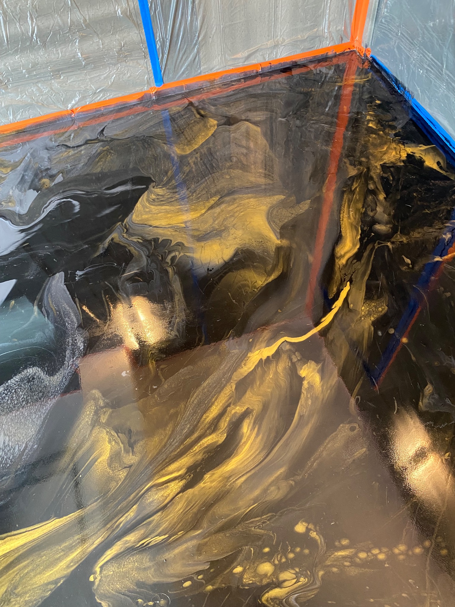 Błyszcząca, czarno-złota posadzka żywiczna z widocznymi krawędziami zabezpieczonymi taśmą malarską, tworząca unikalny wzór.