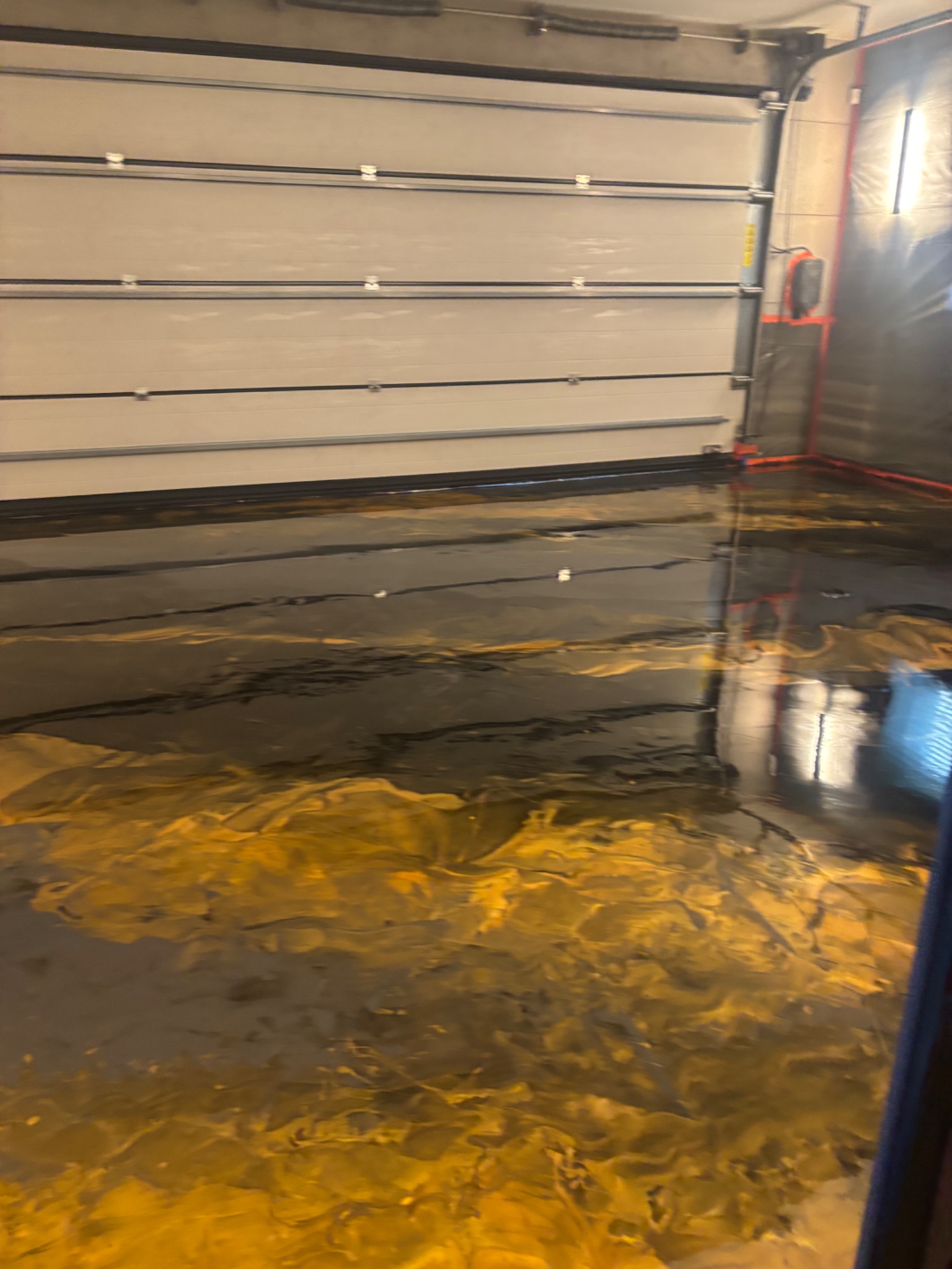 Błyszcząca, złoto-czarna posadzka w garażu z częściowo otwartą bramą segmentową. Efektowna, żywiczna powierzchnia z refleksami światła.