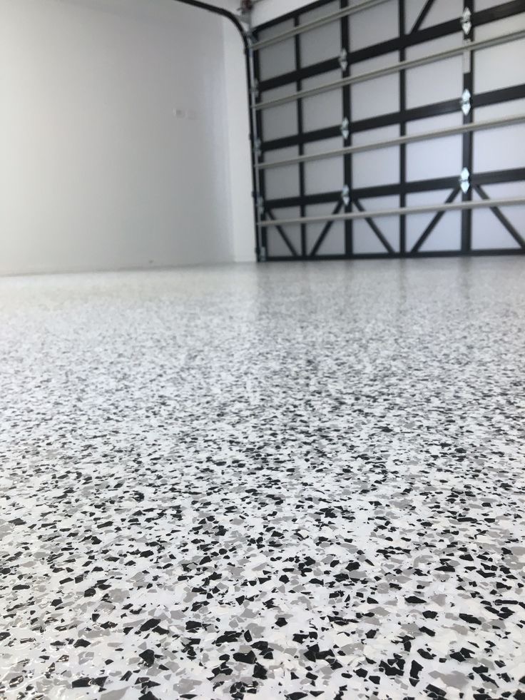 Błyszcząca, jasna posadzka z efektem lastryko w garażu, z otwartą bramą segmentową w tle. Minimalistyczne wnętrze, neutralna kolorystyka.