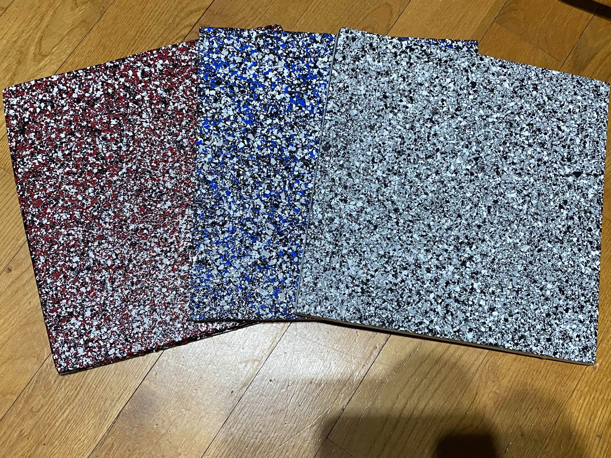 Próbki kolorystyczne posadzek żywicznych z drobnym kruszywem w odcieniach czerwieni, błękitu i szarości, prezentowane w Proszowicach na drewnianej podłodze.