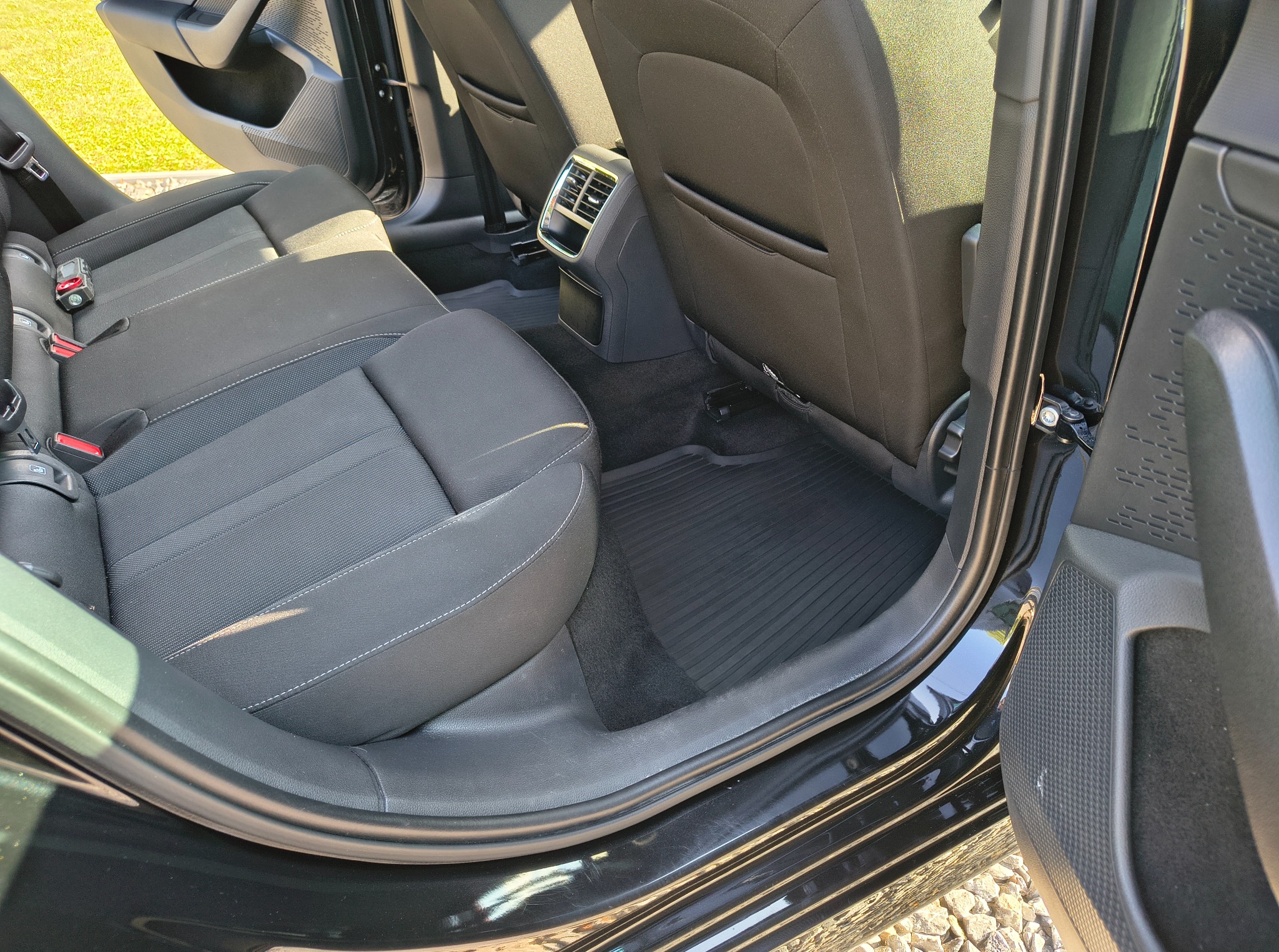 Wnętrze czarnego samochodu z widocznymi tylnymi siedzeniami z szarej tapicerki i czarnymi dywanikami, widziane z otwartych drzwi.