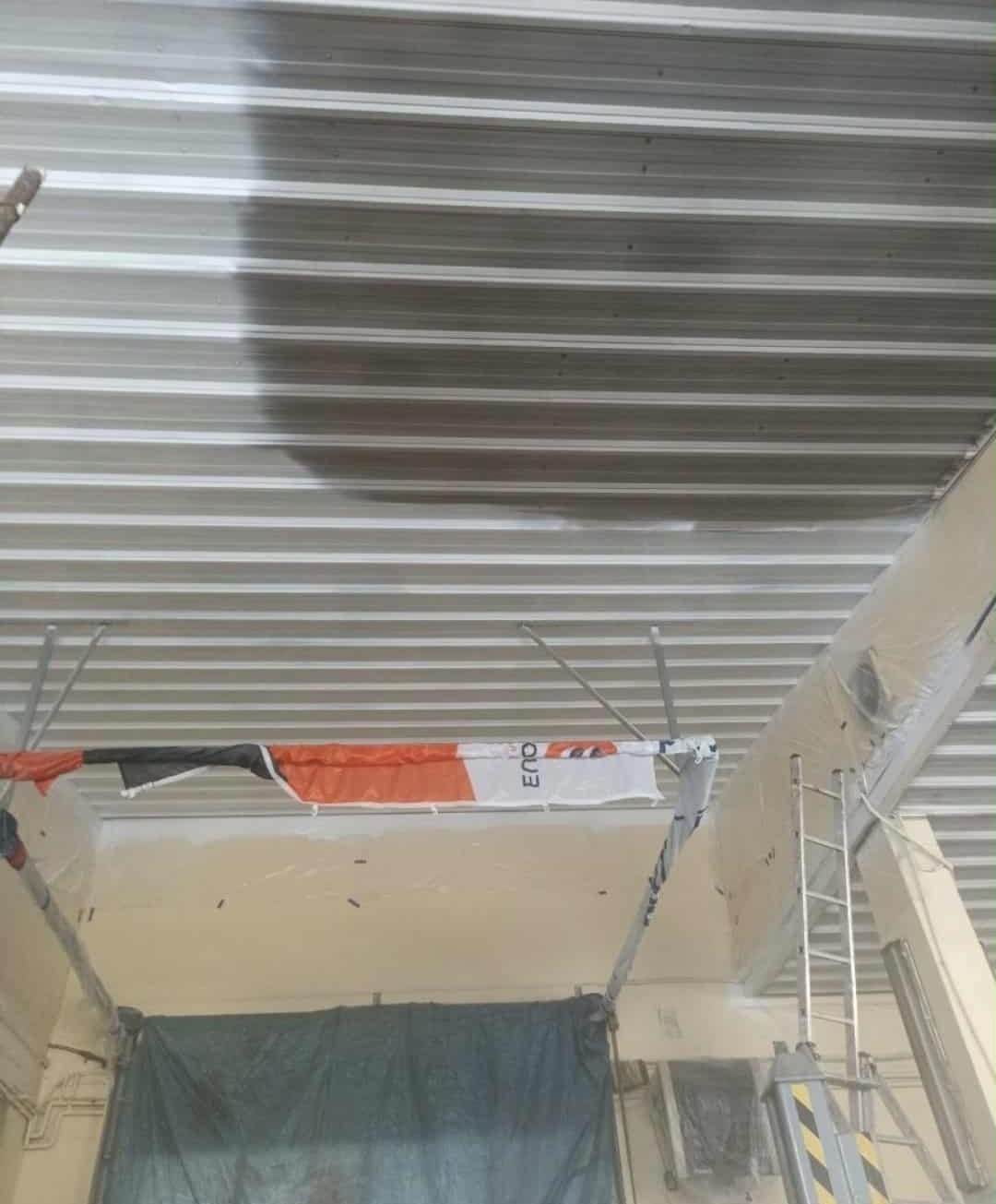 Częściowo pomalowany sufit z blachy trapezowej w hali przemysłowej. Widoczne rusztowanie i zabezpieczenia.