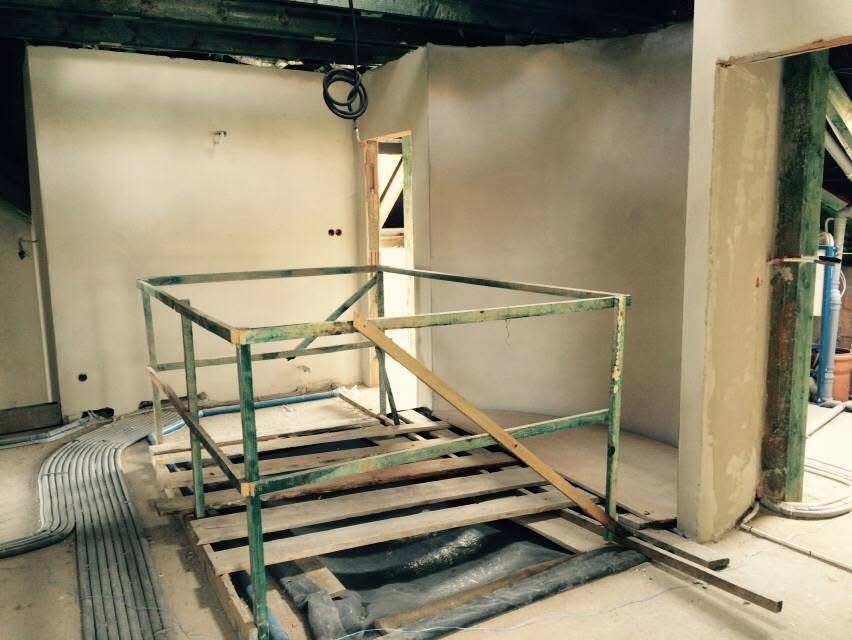 Wnętrze w trakcie prac wykończeniowych: ściany po nałożeniu tynku, widoczne elementy rusztowania i instalacji elektrycznej. Surowy stan, przygotowanie do dalszych etapów.