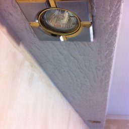 Ekipa malarska - Światło sufitowe z ozdobną ramką w świeżo wykończonym suficie z fakturą, widok z dołu, podkreślający detale wykończenia i oświetlenie.