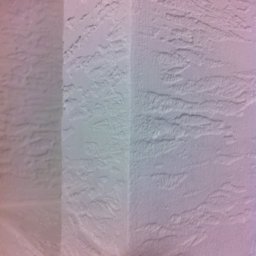 Ekipa malarska - Teksturowana, biała ściana wewnętrzna z widocznym narożnikiem, oświetlona z lewej strony, ukazująca strukturę gładzi w zbliżeniu.