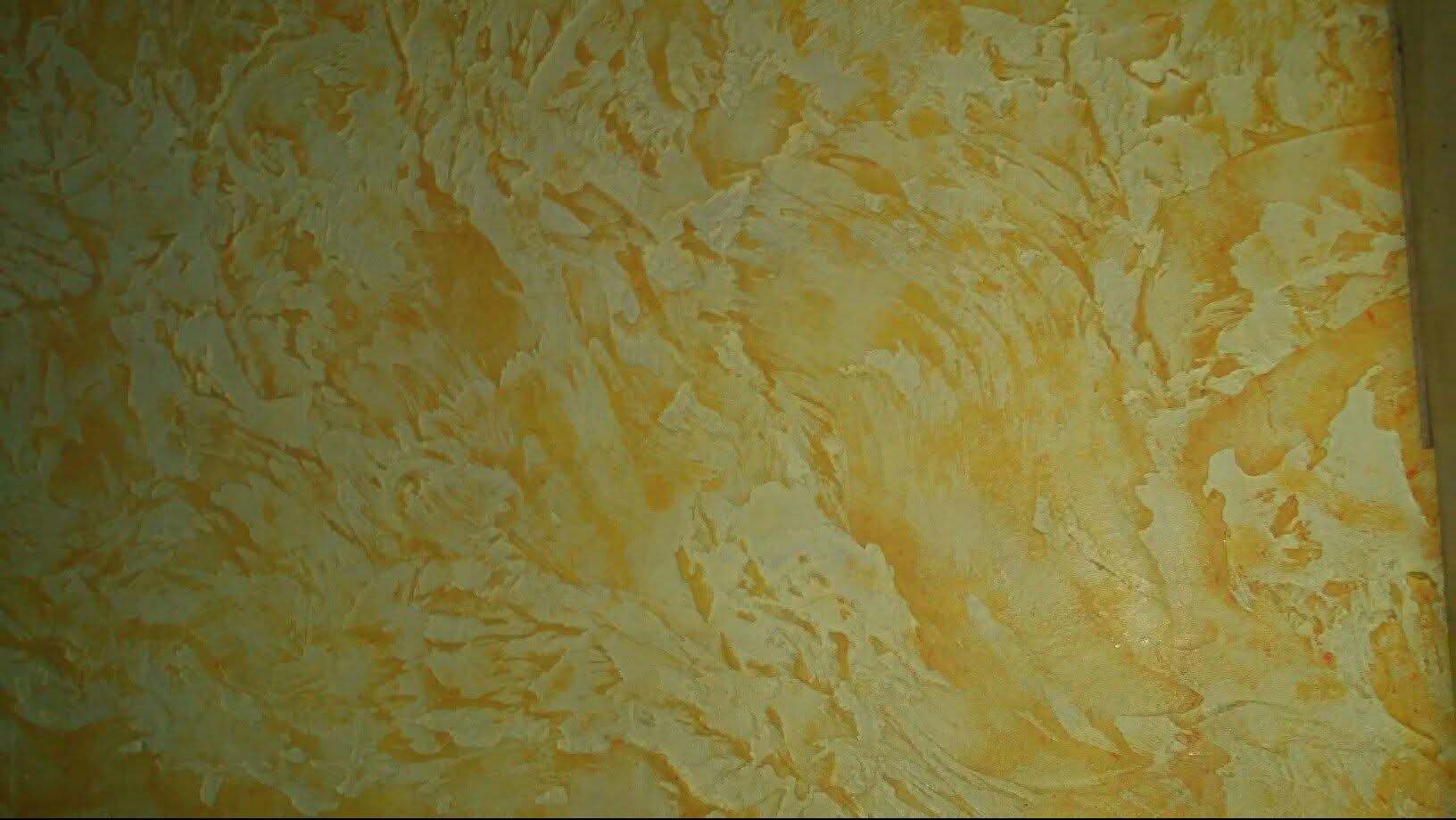 Dekoracyjna, wypukła struktura ściany w odcieniach ciepłego beżu i złota, przypominająca abstrakcyjny pejzaż. Efektowna faktura na ścianie w pokoju.