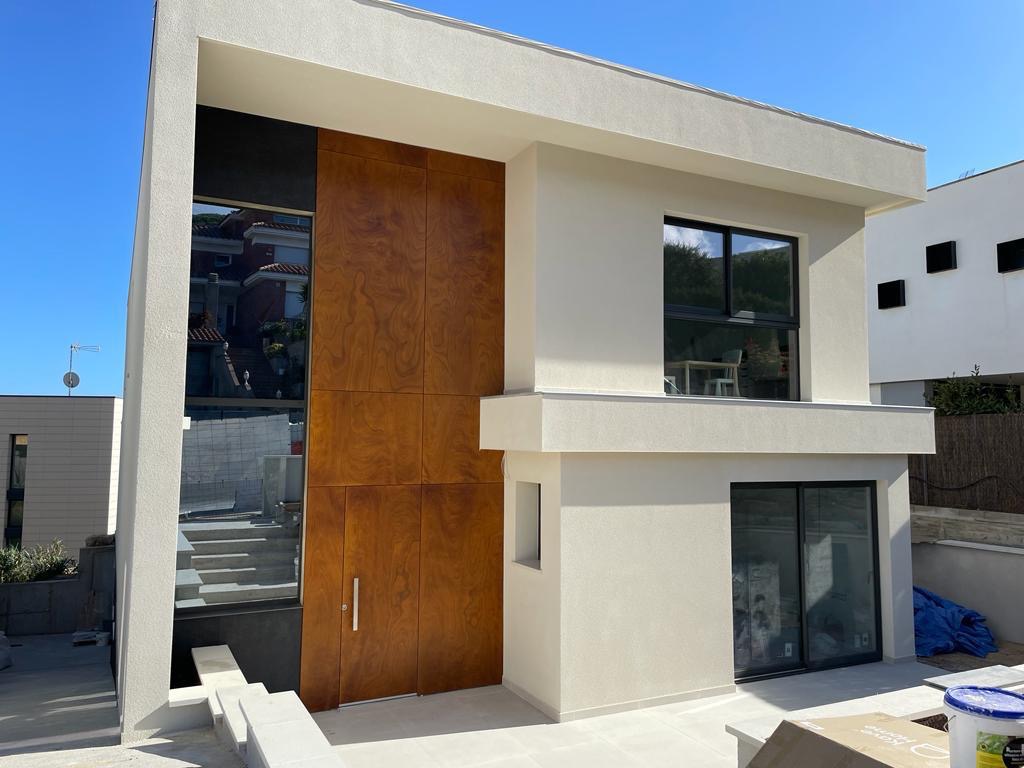 Nowoczesny dom z drewnianą fasadą i dużymi oknami, jasna elewacja, błękitne niebo, minimalistyczny design.