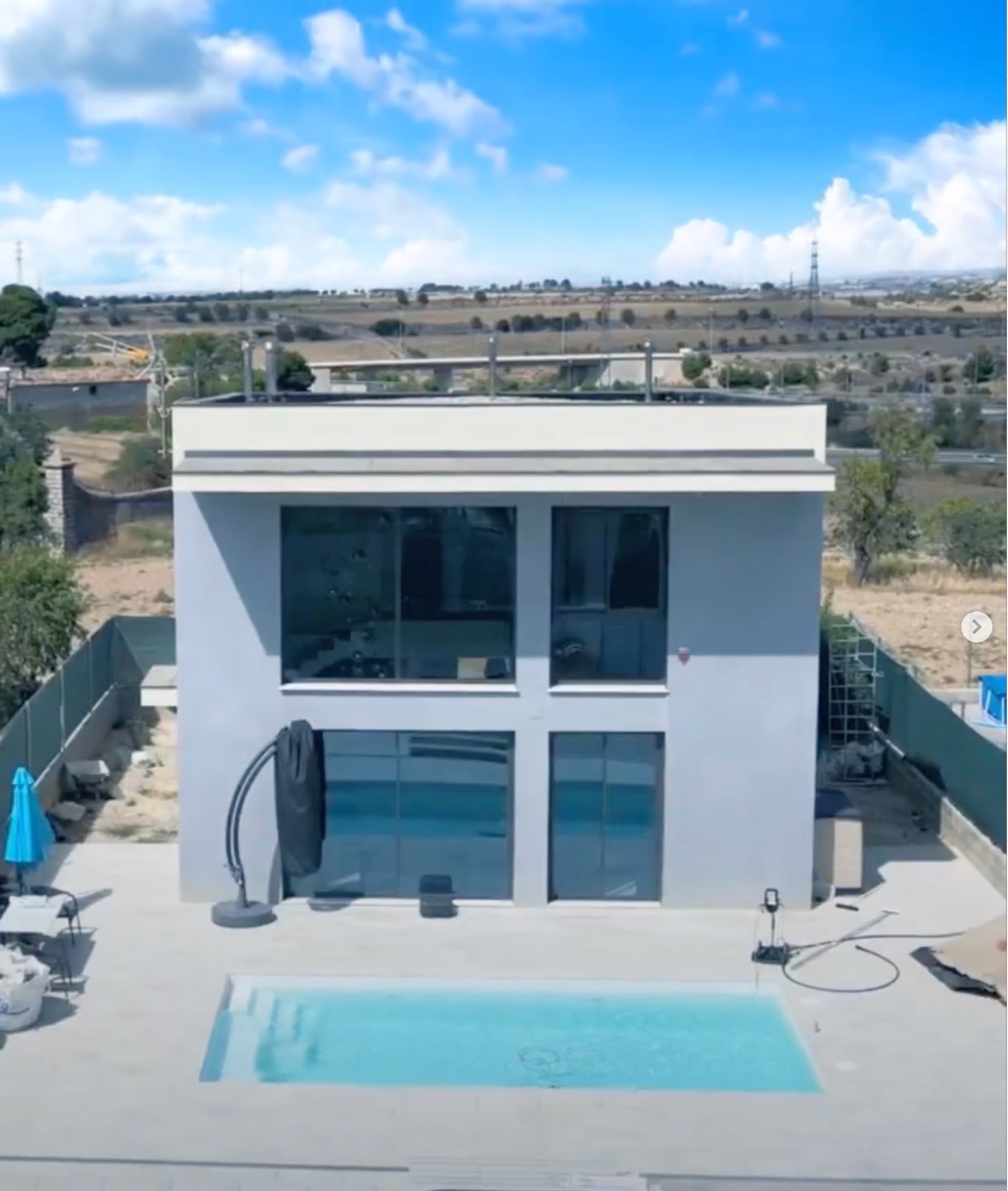 Nowoczesny dom z basenem w Warszawie, widok z góry. Geometryczna bryła budynku, duże okna, minimalistyczny design. Jasne kolory, błękitny basen.