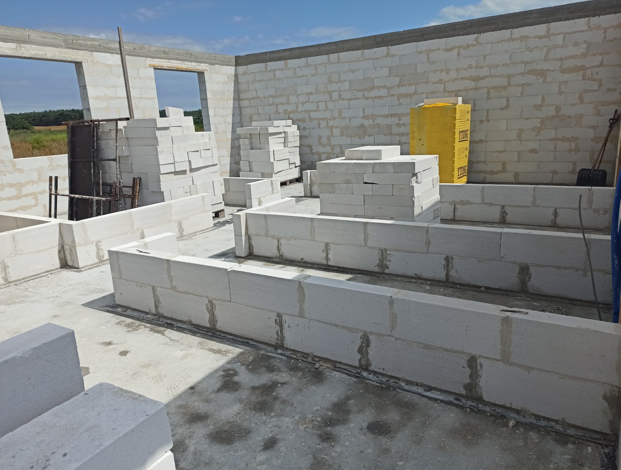 Budowa domu z bloczków Ytong: widok na fundamenty i ściany w trakcie wznoszenia. Na pierwszym planie ułożone bloczki, w tle okna i narzędzia.